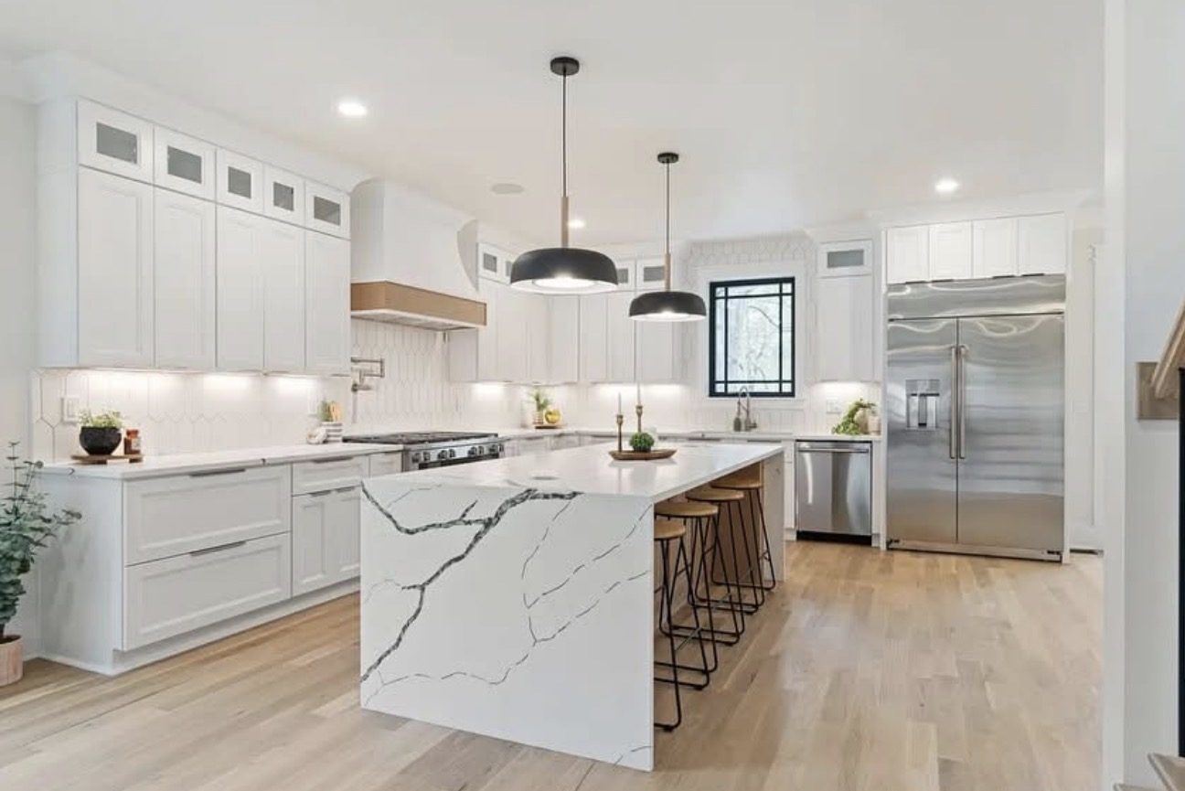 White kitchen with a waterfall-edge quartz island, custom hood, and stainless appliances.