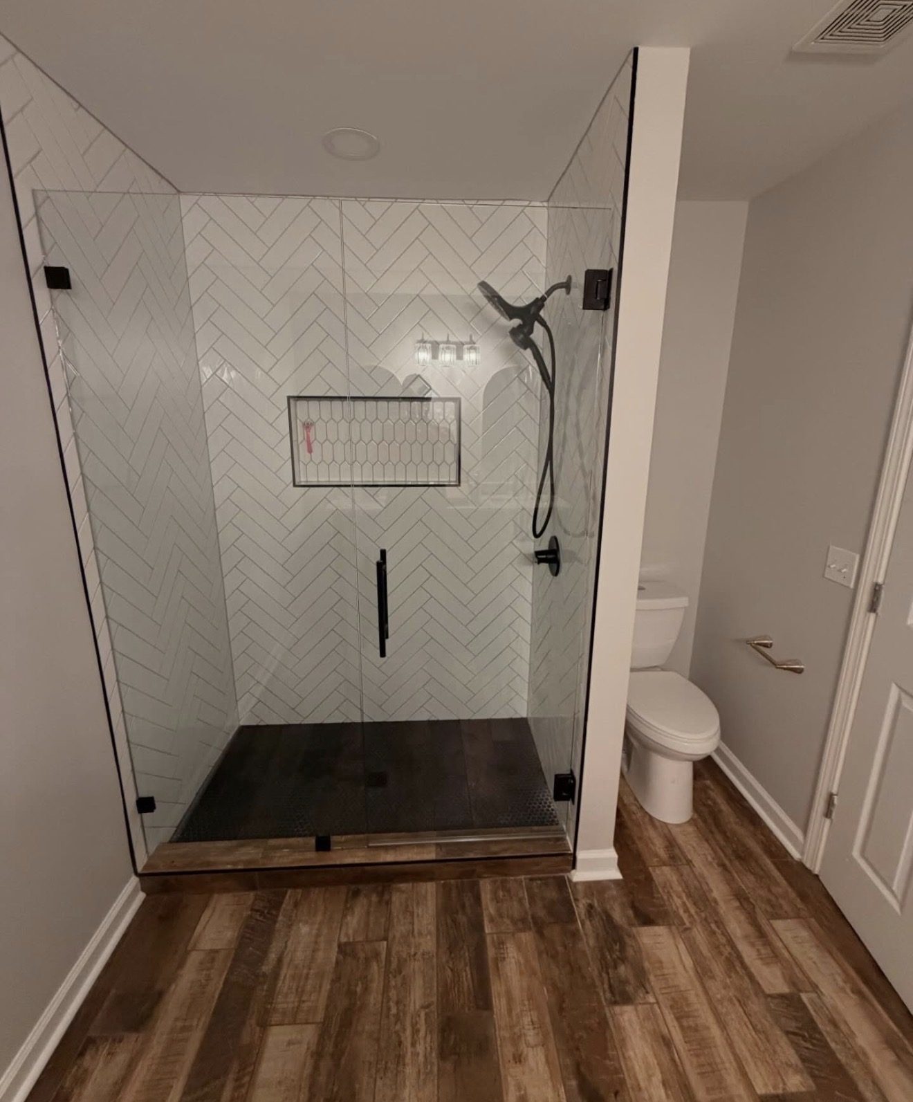 Walk-in shower with herringbone white tile, a recessed niche, and frameless glass doors.